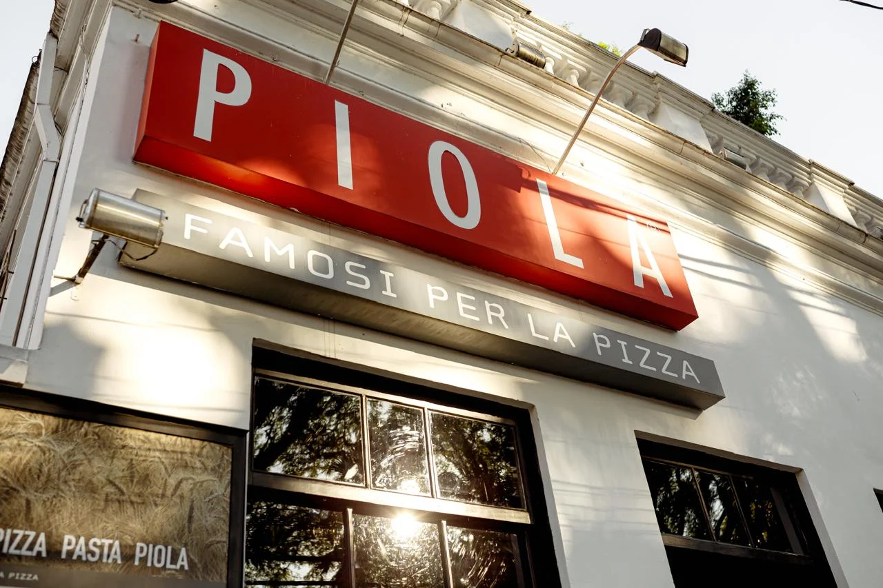 Fachada da Piola com letreiro vermelho neon famoso pela pizza