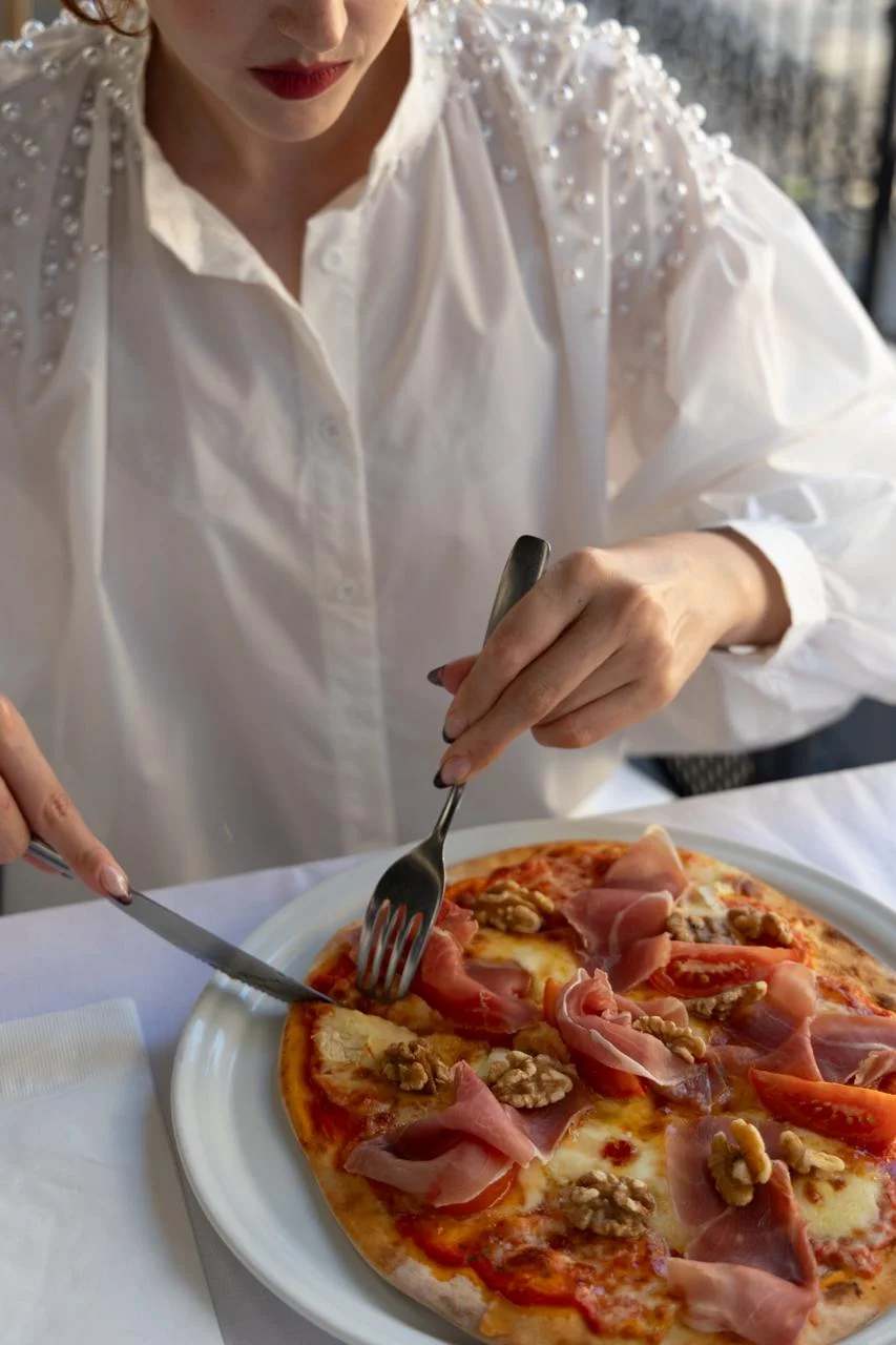 Mulher degustando pizza com presunto e castanha de caju